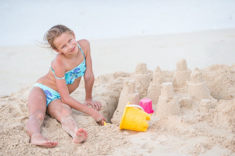 Adorable little girl playing with beach toys on white tropial beach