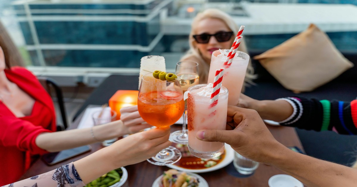 Group of friends raising cocktails at a rooftop bar during a bachelorette party at sunset