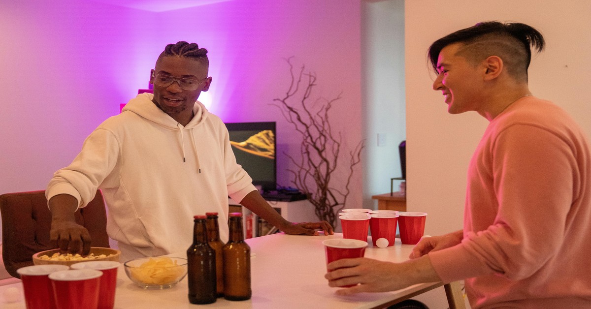 Two men sitting at a table with beers and a notebook, discussing plans for a bachelor party