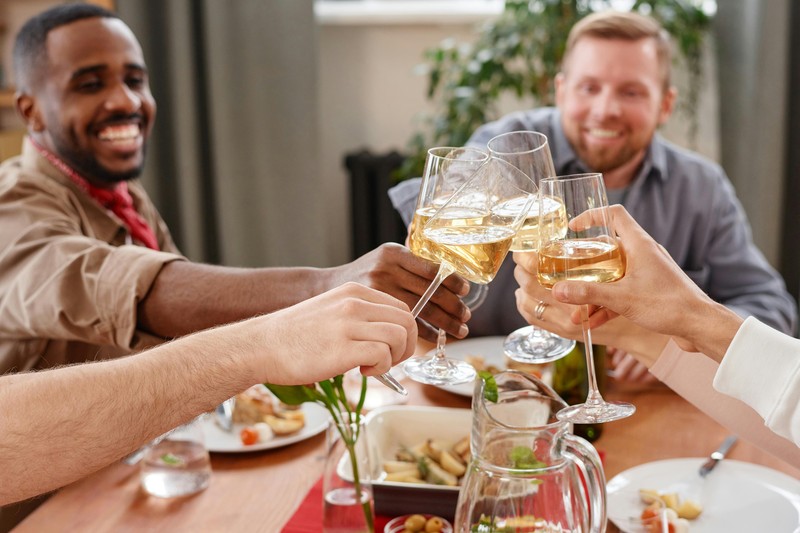Best man raising a glass of whiskey to make a toast at a dinner table with friends