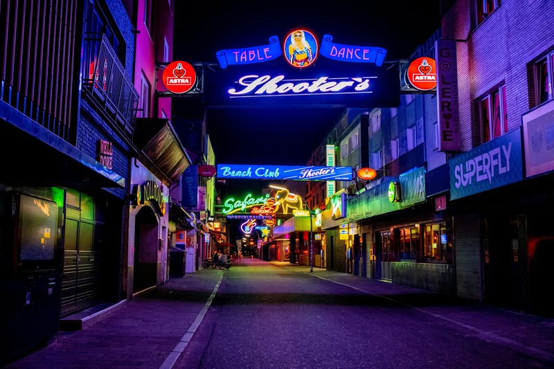 Walkable city street lined with bars and glowing signs at night