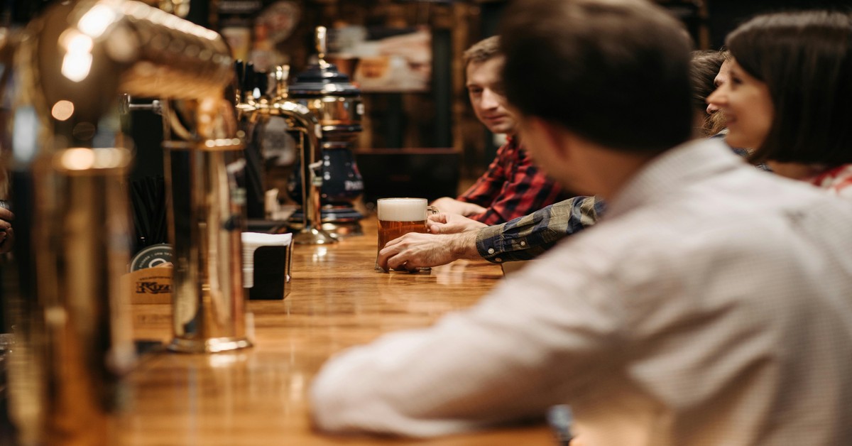 Group of friends laughing and holding drinks at a crowded bar during a pub crawl