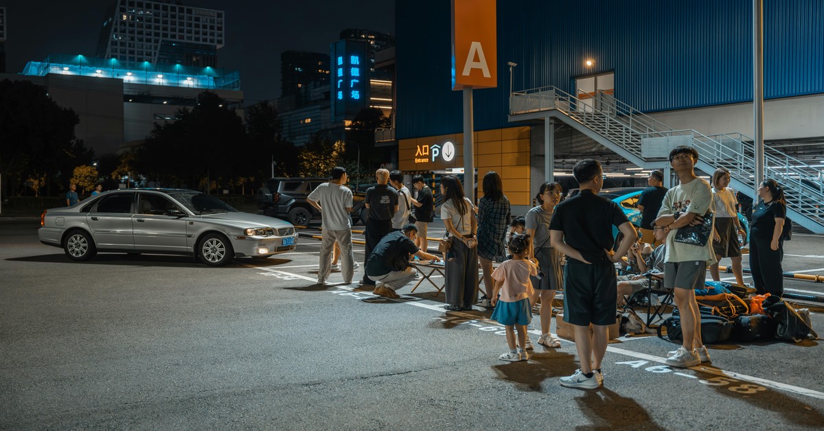 A large group of friends waiting for a ride-share car on a bustling city street at night