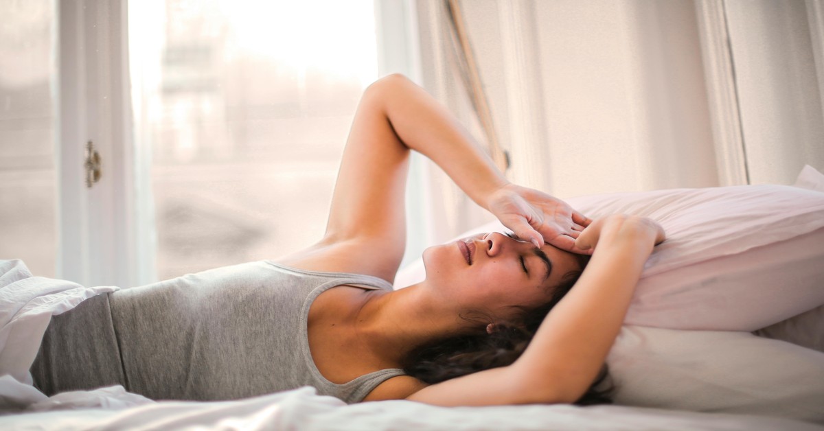 Waking Up with a Travel Hangover in a Hotel Room person waking up in a hotel bed with sunlight coming through curtains, holding head