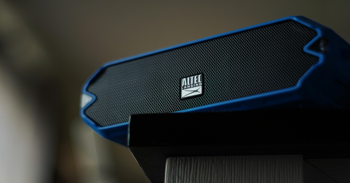 A portable bluetooth speaker playing music in a backyard party setting with people around